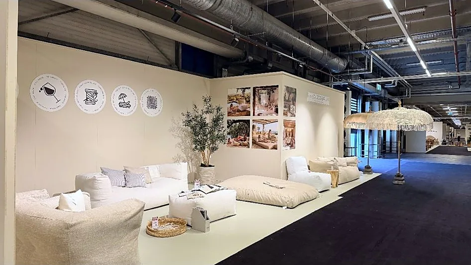 Onze stand bij TICA Projects Venlo met loungebank, poefs en een liggend kussen rond een kunstolijfboom, met een macramé parasol met franjes ernaast en moodboards aan de wand